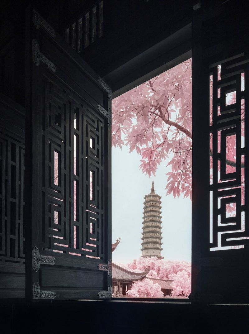Framed by a window, the pagoda at Bái Đính Temple in Vietnam stands out against a clear sky, an infrared filter giving the foliage of surrounding trees a pink hue.