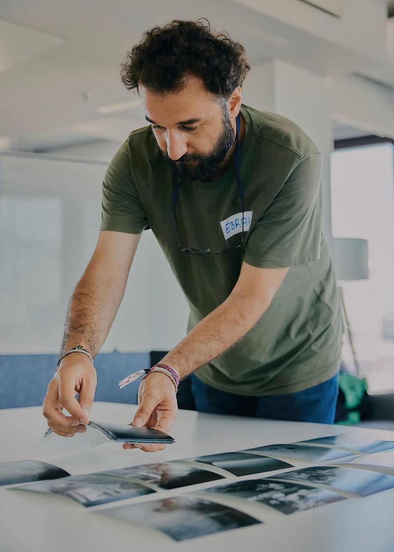 Photojournalist Ebrahim Alipoor leans over a table, placing out rows of photographs.