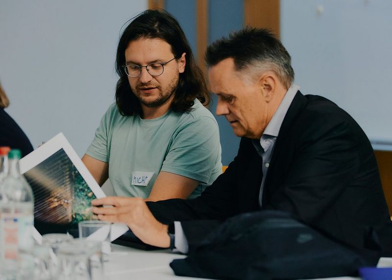 Michał Siarek discusses his work with another man seated beside him at a table.