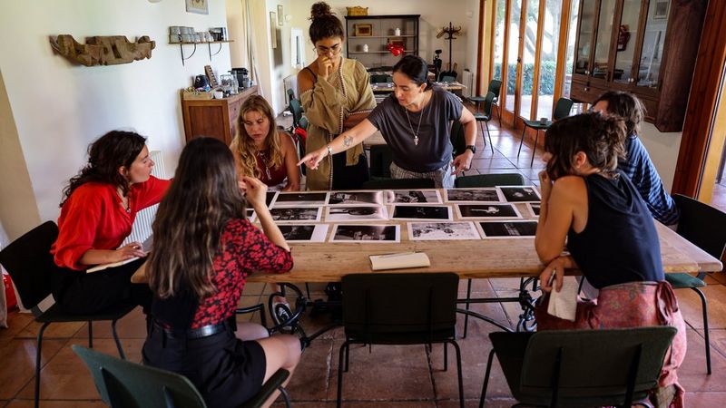 A group of people around a wooden table looking at portfolio photographs.