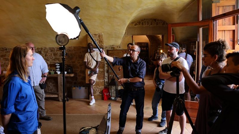 A group of people indoors taking pictures with a Canon camera of a woman in a blue shirt, photographer Paolo Verzone adjusting a lighting rig above her.