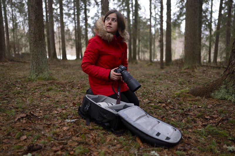 Wildlife photographer Dani Connor holding a Canon EOS R6 Mark III as she kneels next to her camera bag on a forest floor.