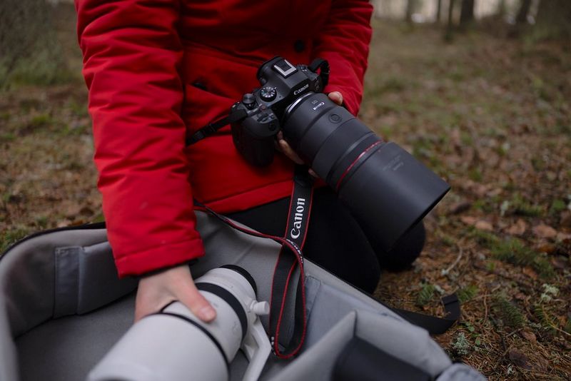 Wildlife photographer Dani Connor reaches for a Canon telephoto lens in her camera bag on a forest floor.