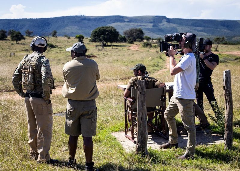 Daniel Bateman stands holding a Canon Cinema EOS camera, with four other figures next to him, looking our over grasslan
