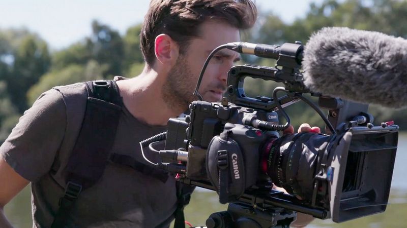 DoP Ben Sherlock filming with the Canon EOS C300 Mark III in a rural setting with bushes and water in the background.
