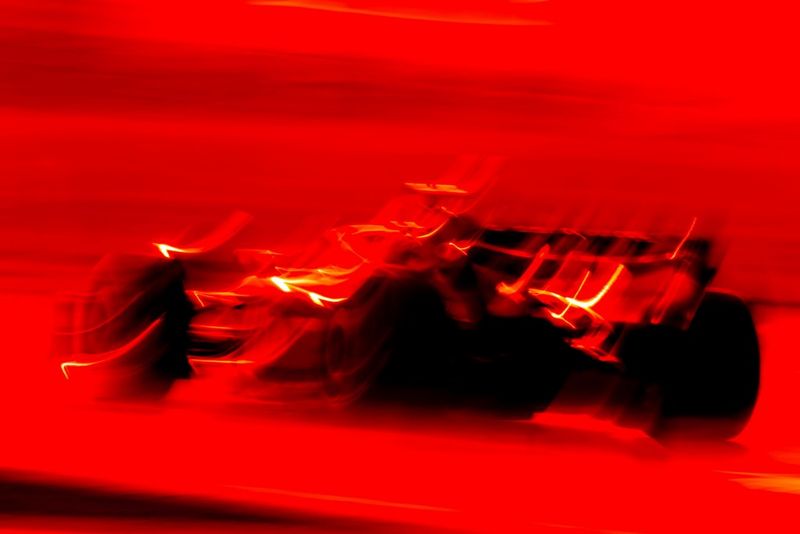 Een Formule 1-raceauto tegen een rode achtergrond, vastgelegd met een lange sluitertijd om onscherpe lijnen te creëren voor een artistiek effect. Gefotografeerd met een Canon EOS R5 door Frits van Eldik.