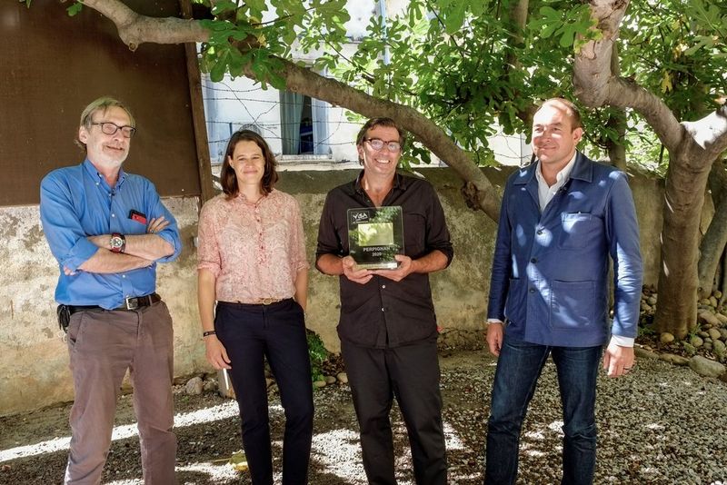 In a shaded courtyard, a man dressed all in black holds an award, standing with two men and a woman who are all smiling at the camera. The people are Jean-François Leroy, Claire-Anne Devillard, Michaël Zumstein and Lucas Menget.