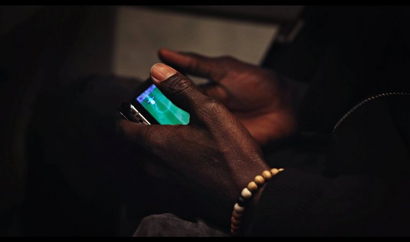 A person watches football on their phone in this still from Camille Millerand's documentary short, The Invisibles. 