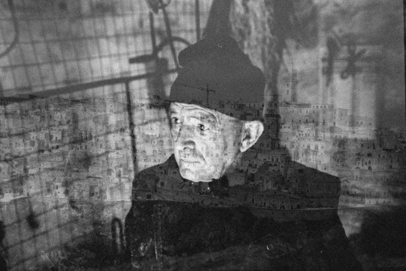 A black and white double exposure of an elderly man in a hat and a cityscape of old stone buildings.