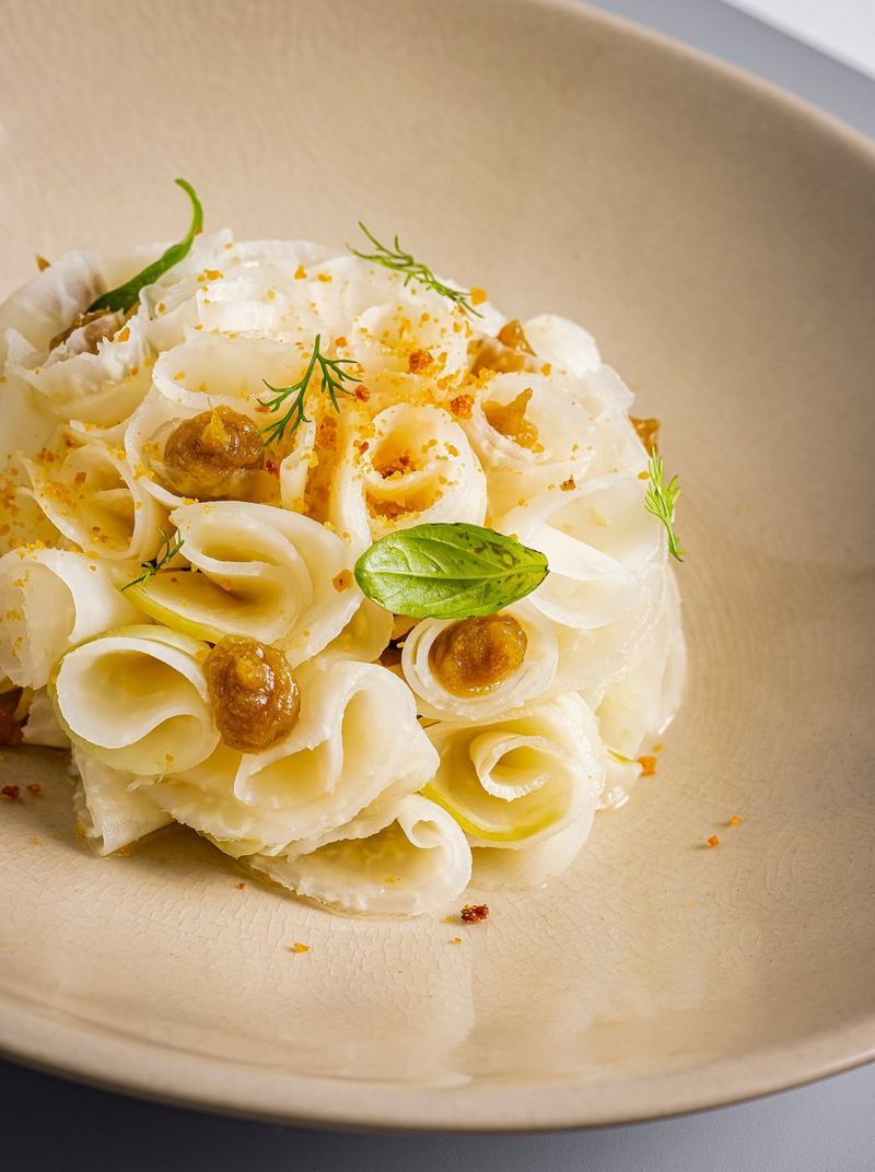 Thin ribbons of salsify tucked into a neat ball garnished with green leaves and dots of puree. Shot on Canon.