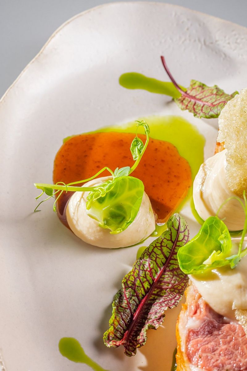 A mound of thick sauce sitting on a small pool of chili and lime sauce garnished with leafy greens on a white plate. Shot on Canon.