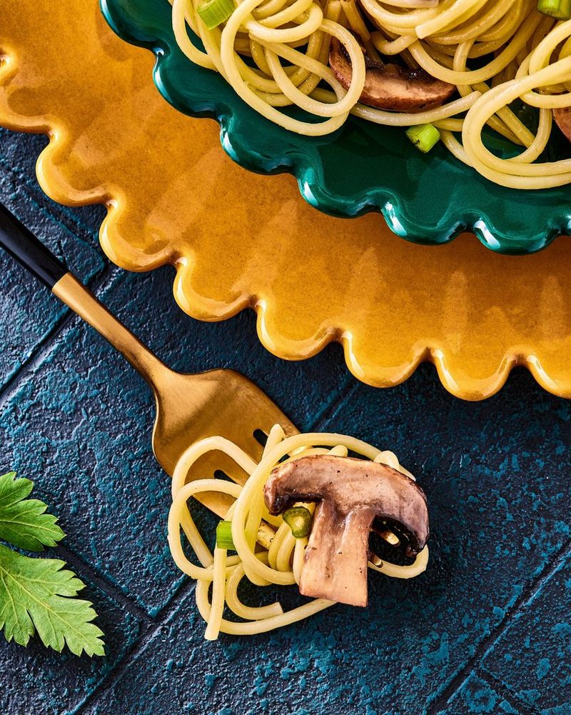 A golden fork entwined with spaghetti with a cut mushroom on top. Shot on Canon.