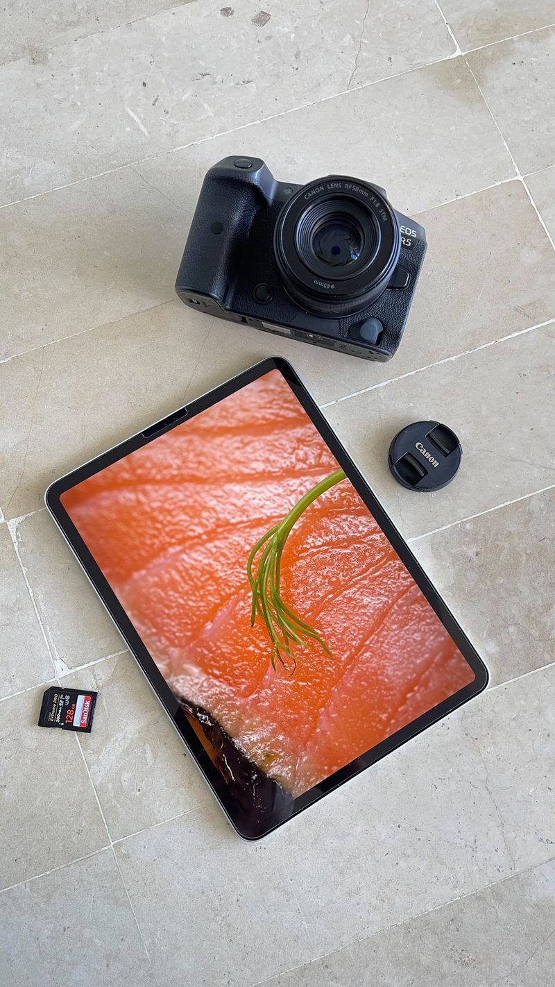 Overhead view of a tablet displaying a macro shot of salmon next to a Canon camera and SD card laid on a stone floor. Shot on Canon.