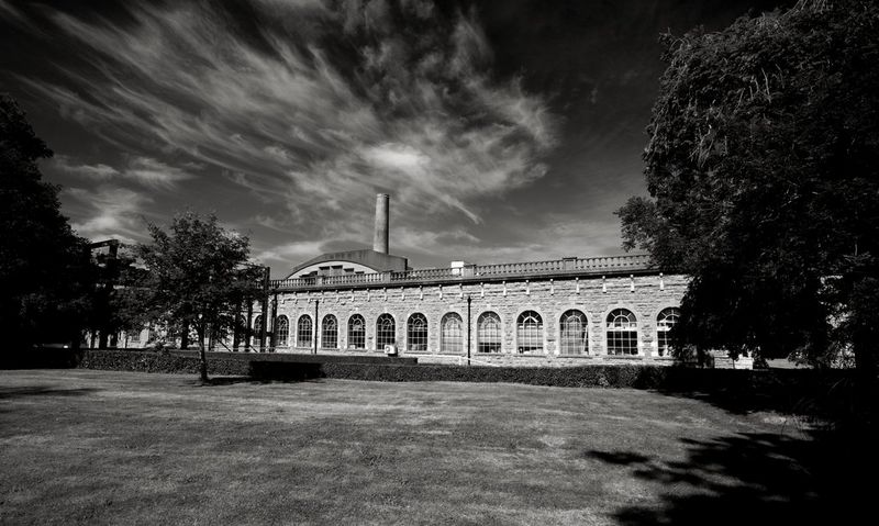 Une usine de papier bordée de fenêtres se dresse sous un voile de nuages, précédée d'un espace vert ouvert.