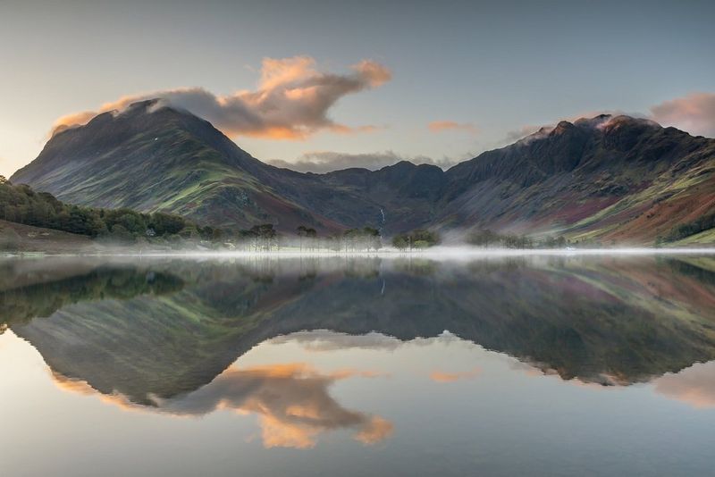 Une belle montagne rocheuse couverte de feuillage et d'herbe se dresse au sommet d'un lac à Buttermere, dans le Lake District. La montagne se reflète dans l'eau paisible. Photo prise avec un appareil Canon.
