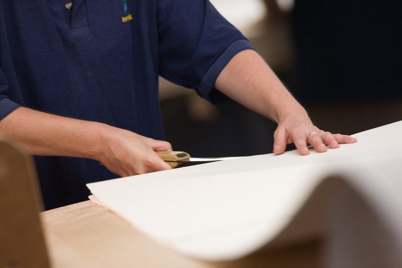 Un ouvrier de St Cuthberts Mill tient une pile de papier pendant qu'il la tranche avec un couteau de l'autre main, dans le cadre du processus de découpage des bords. Photo prise avec un appareil Canon.