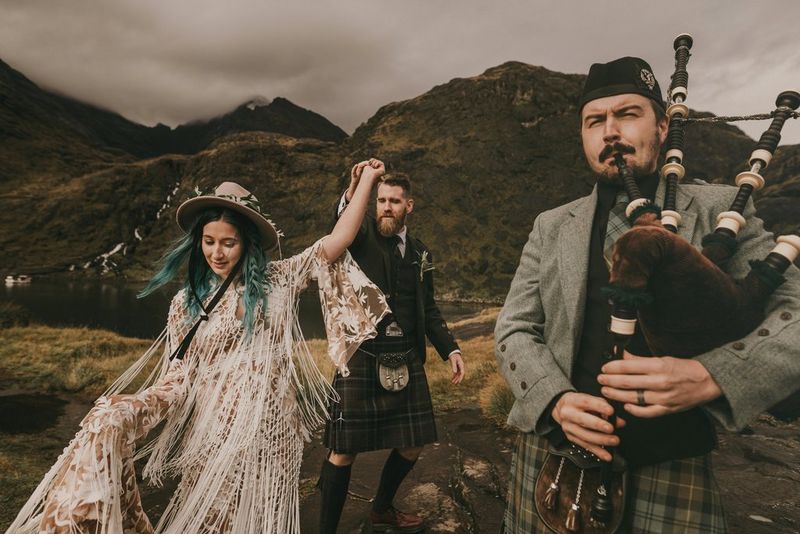 Una coppia di sposi balla su una collina vicino ad un uomo che suona la cornamusa.