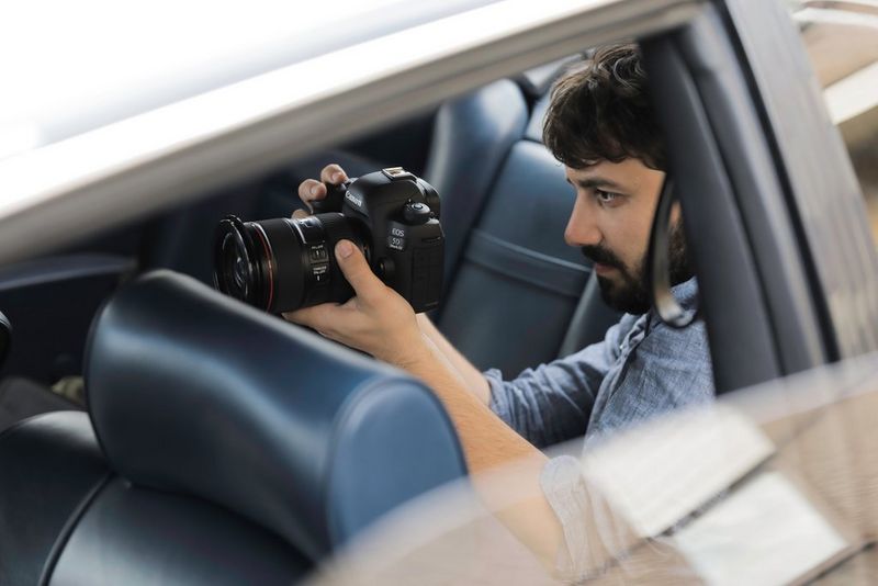 Cinematographer Christian Anderl in the rear seat of a motor car, filming with a Canon EOS 5D Mark IV.