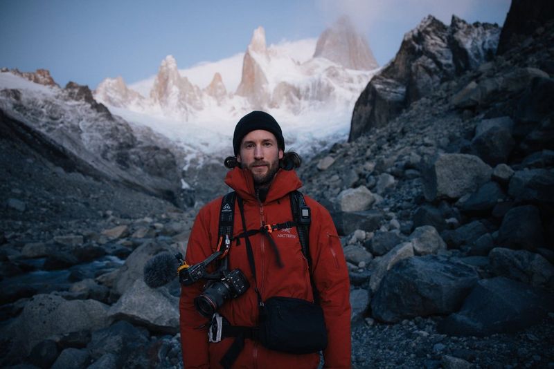 Daniel Ernst in front of a mountain in Patagonia, a Canon EOS C50 attached to his backpack strap.