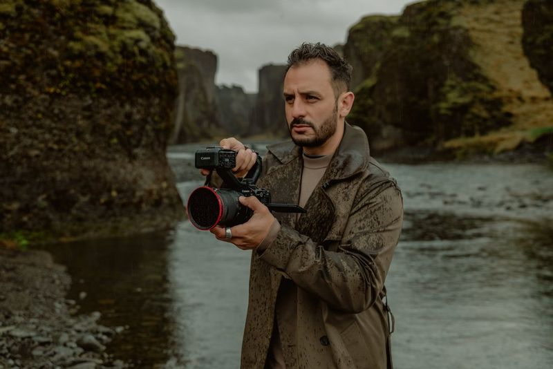 Luã Araújo holds a Canon EOS C50 by the top handle, filming in wet conditions in Iceland.