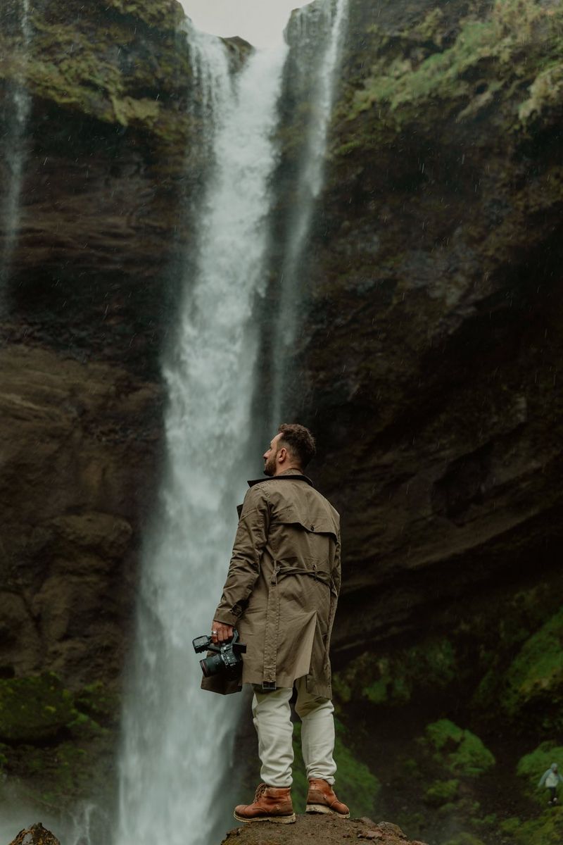 Filmmaker Luã Araújo stands in front of a waterfall in Iceland, holding a Canon EOS C50 by his side.