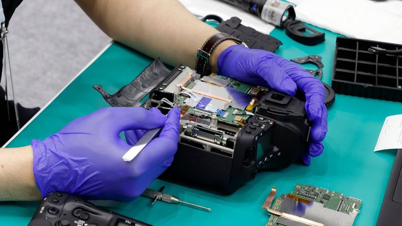 De gehandschoende handen van een technicus die onderhoud verricht aan de binnenkant van een Canon-camera.