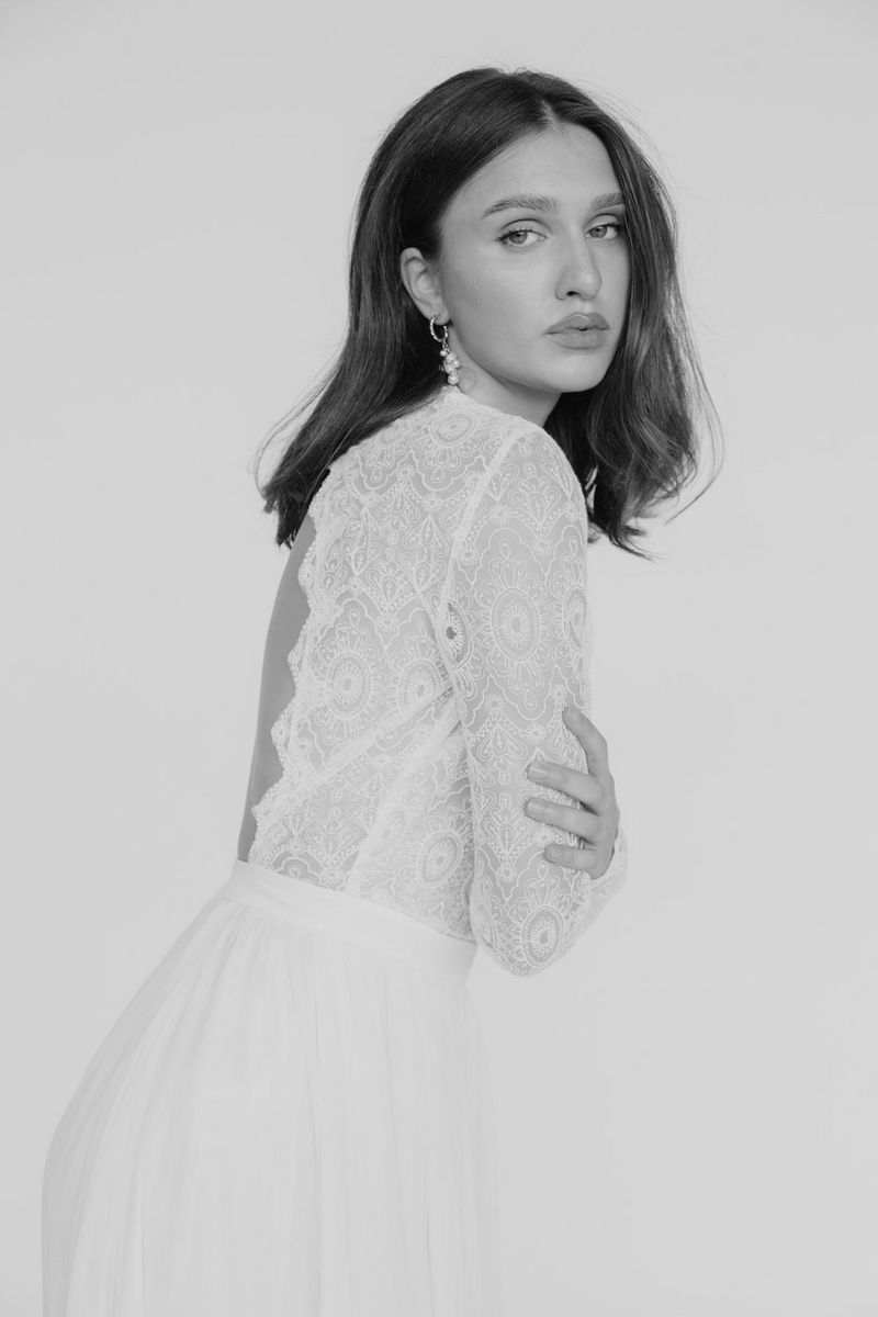 Een donkerharig model in een witte bruidsjurk kijkt naar de camera terwijl ze van de zijkant is gefotografeerd met haar armen over elkaar geslagen. Gefotografeerd door Julia Blumenthal en Gil Gropengießer met een Canon EOS R6 Mark II.