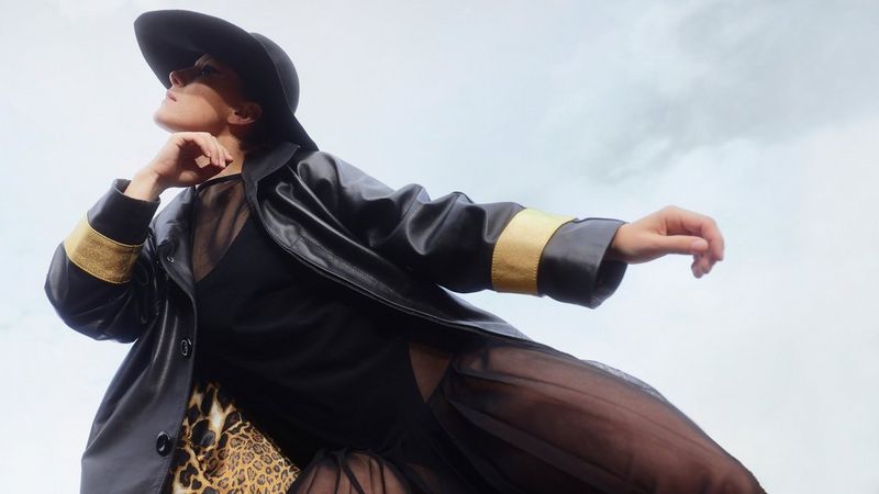 Een vrouw in opvallende zwart-goudkleurige outfit leunt naar rechts, en houdt hand en arm tegen haar borst. Gefotografeerd door Nana en Juhana Simelius met een Canon EOS R6 Mark II.