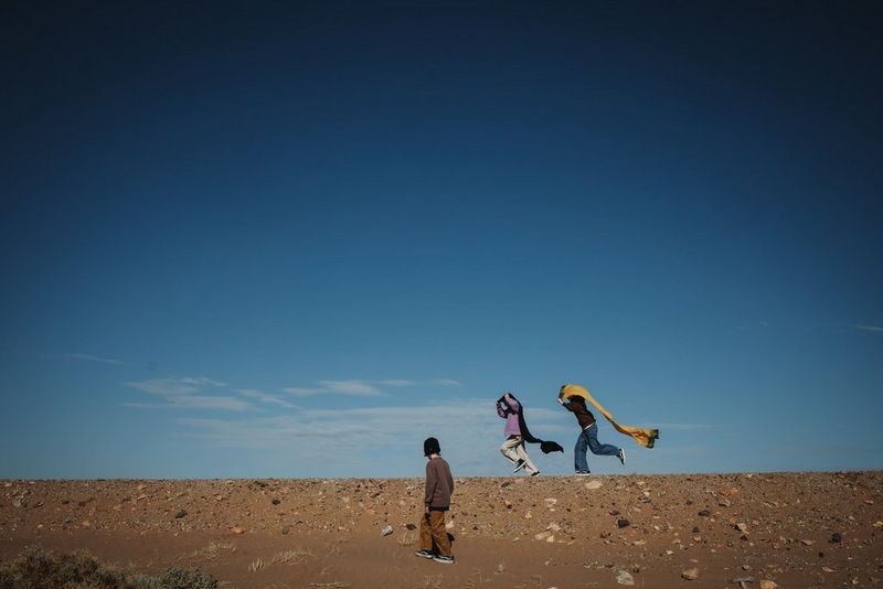 Two figures run along the sand, with a third figure watching, in a photo by Marisa Martins taken on a Canon EOS R8. 