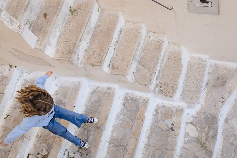 A child is captured from above, jumping down steps to the beach, in a photo by Marisa Martins taken on a Canon EOS R8.