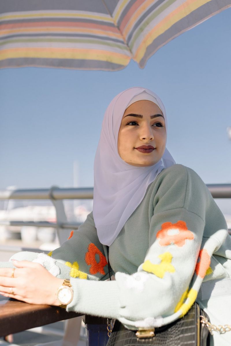 A woman sits outdoors at a table with an umbrella overhead in a photo by Aline Deschamps taken on a Canon EOS R8.