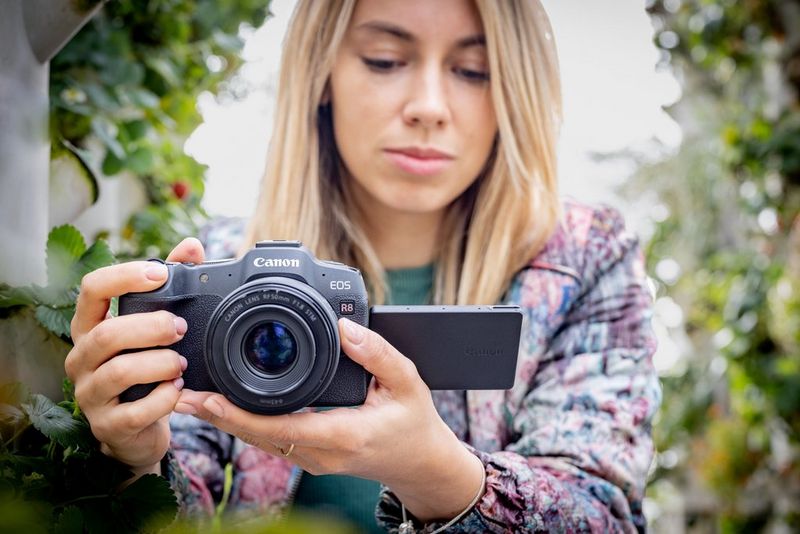 Een vrouw houdt een Canon EOS R8 vast en kijkt op het scherm.