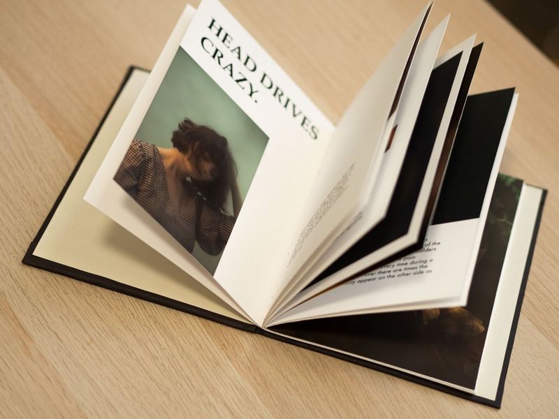 A handcrafted zine placed on a table, open on a page showing a young woman holding her hand on her head.