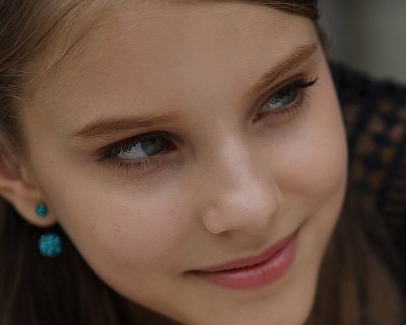 Een detail van een scherpere maar verder vrijwel identieke foto van een jonge vrouw die uit het raam leunt en opzij kijkt.