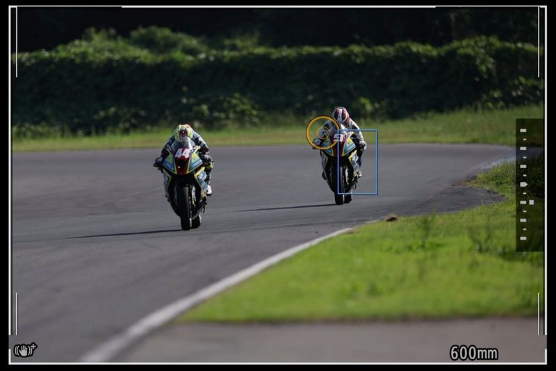 Due moto in corsa viste attraverso il mirino. Sulla moto posteriore vi sono un cerchio arancione e un rettangolo blu.