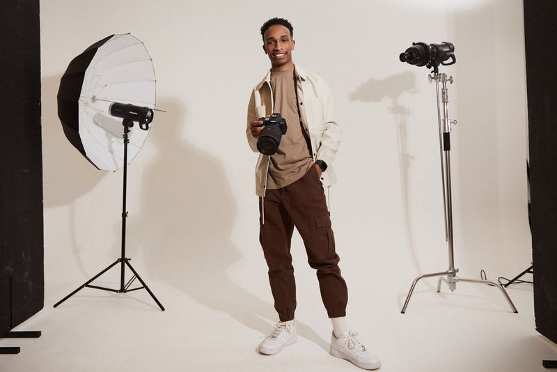 Fotograful de modă Ian Hippolyte aflat într-un studio, între două instalaţii de lumini de studio, ţinând în mână un aparat foto Canon EOS R5.