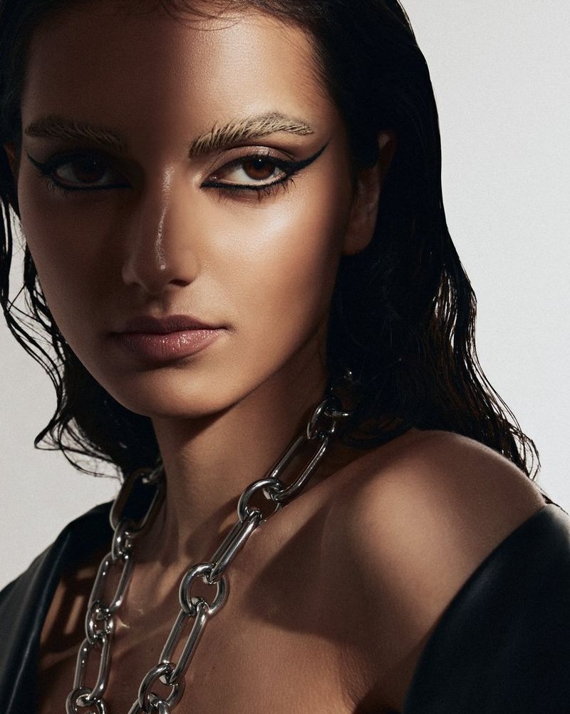 Полоса света падает на лицо модели с ярким макияжем и большим ожерельем на этом портрете крупным планом.