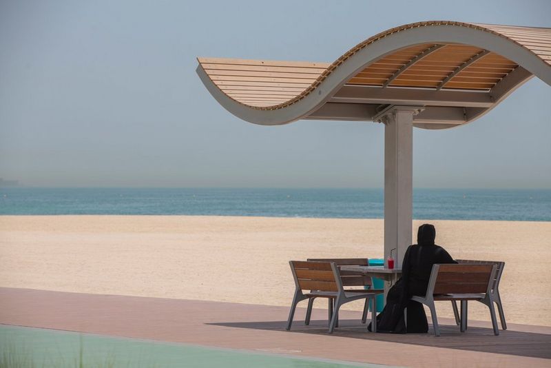 A woman in a burka sits at a beachside café, looking out to sea.