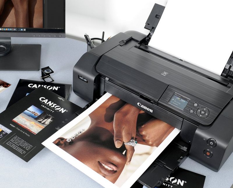 A sheet of Canson® Infinity fine art paper emerges from a Canon PIXMA PRO-200 printer. The print of a woman's face is cropped just above the mouth and she is wearing long diamond earrings and a diamond ring 