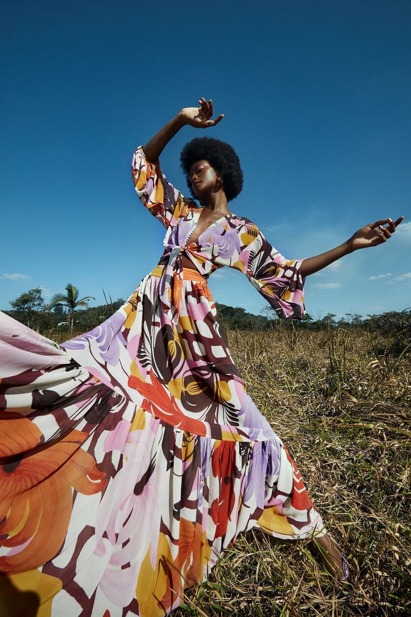 A woman in a colourful dress dancing in a field under blue skies.