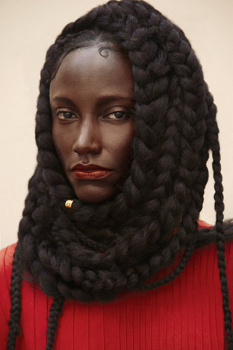 A woman in a red jumper with a long braid wrapped several times around her neck and head.
