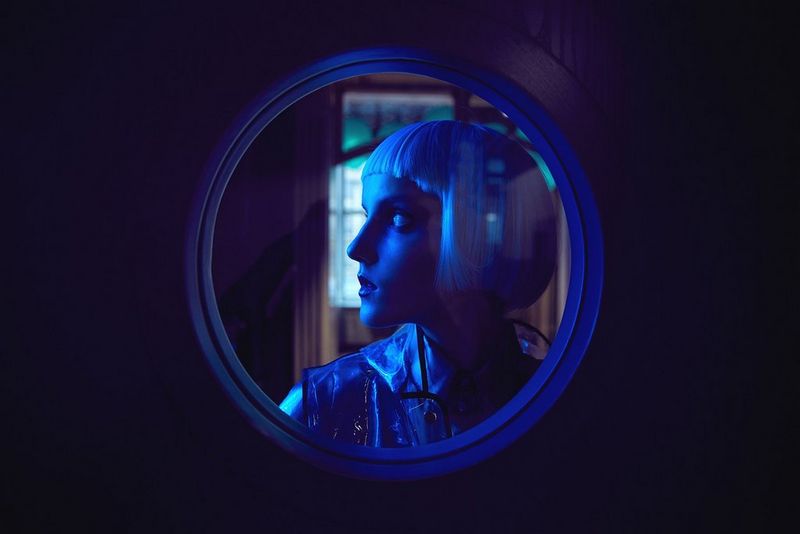 A woman looks sideways in a blue-lit photograph.