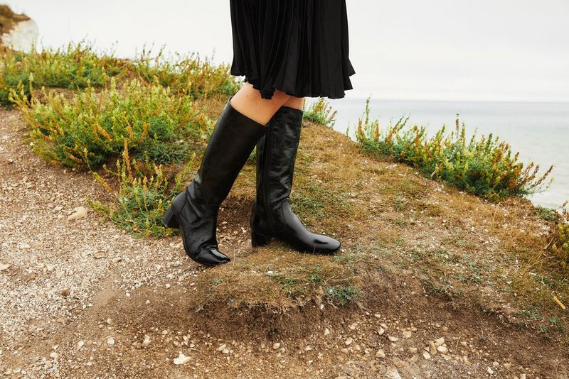 Jambes recouvertes d'une jupe sombre et chaussant des bottes noires au bord d'une falaise. Photo prise par Kid Circus.