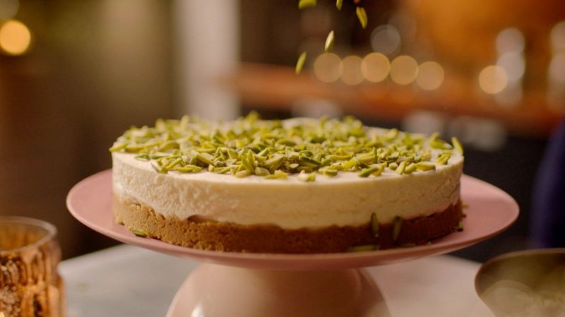 Una sontuosa cheesecake guarnita con delle noci poggiata su un piatto rosa chiaro.