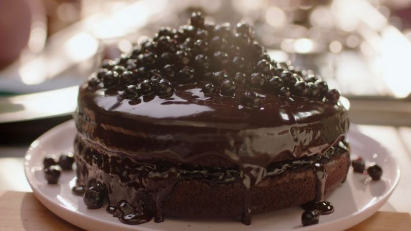 Un'elaborata torta al cioccolato ricoperta di glassa al cioccolato e guarnita con ribes neri.