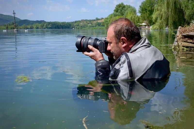 Filmmaker Roberto Palozzi standing chest deep in a lake with his Canon camera. 
