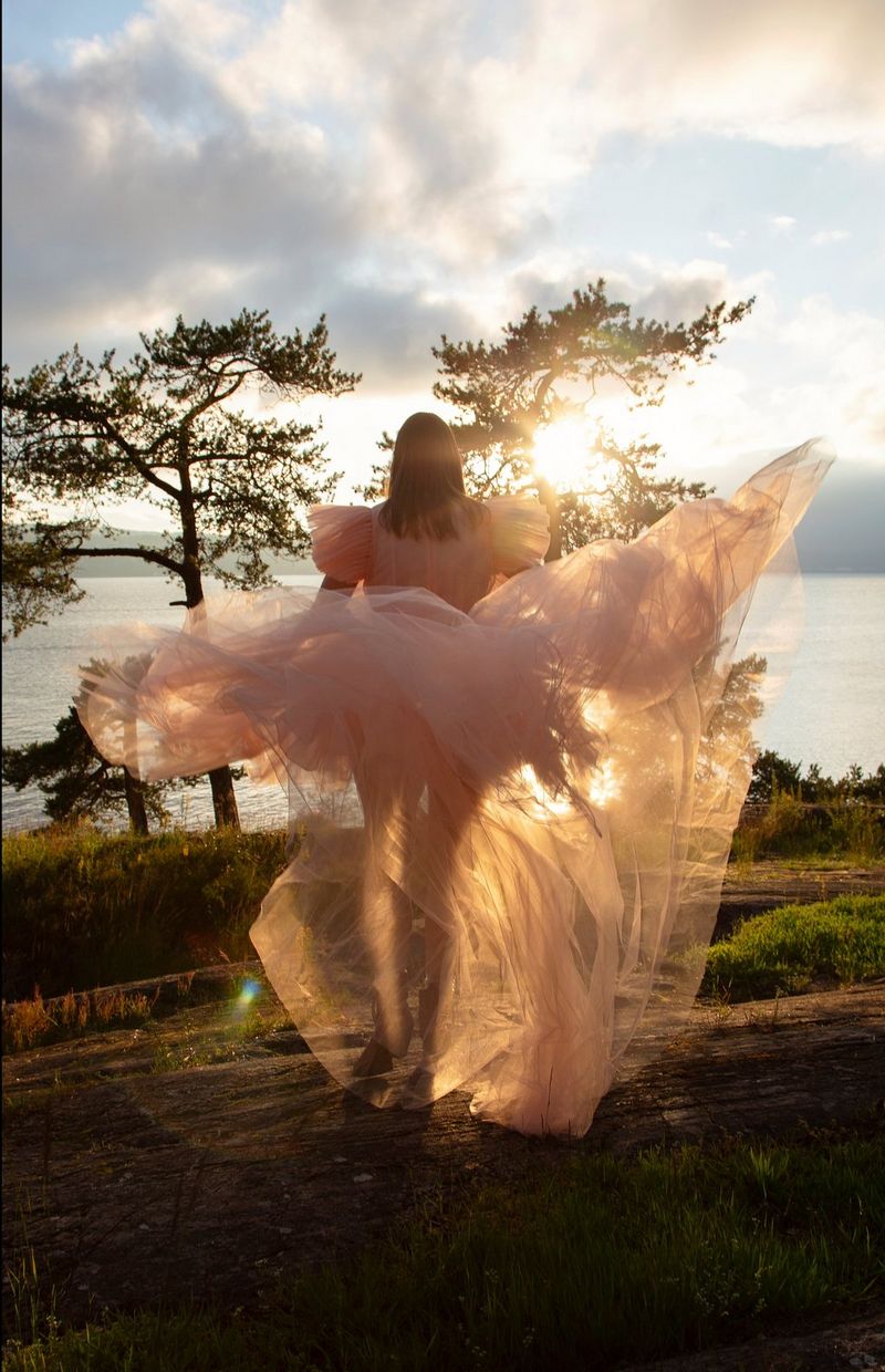 Una donna con un lungo abito fluttuante corre verso una distesa d'acqua dando le spalle alla fotocamera.