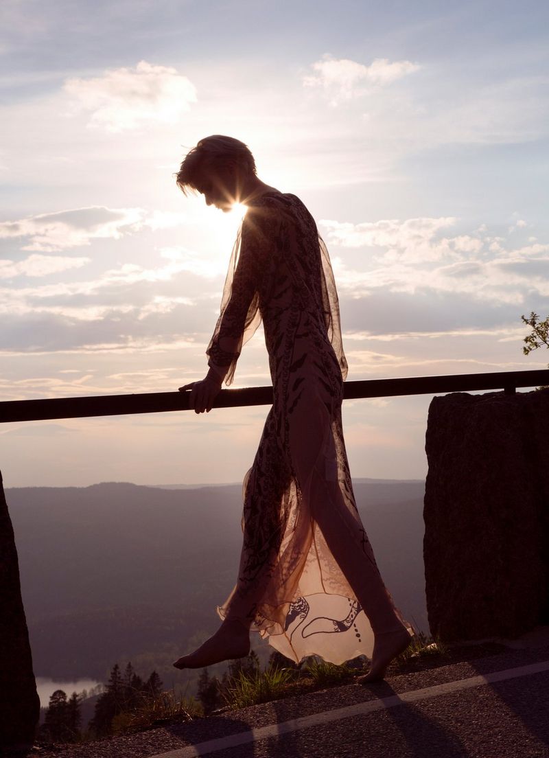 Una donna con un abito vaporoso guarda il paesaggio sottostante da una barriera.