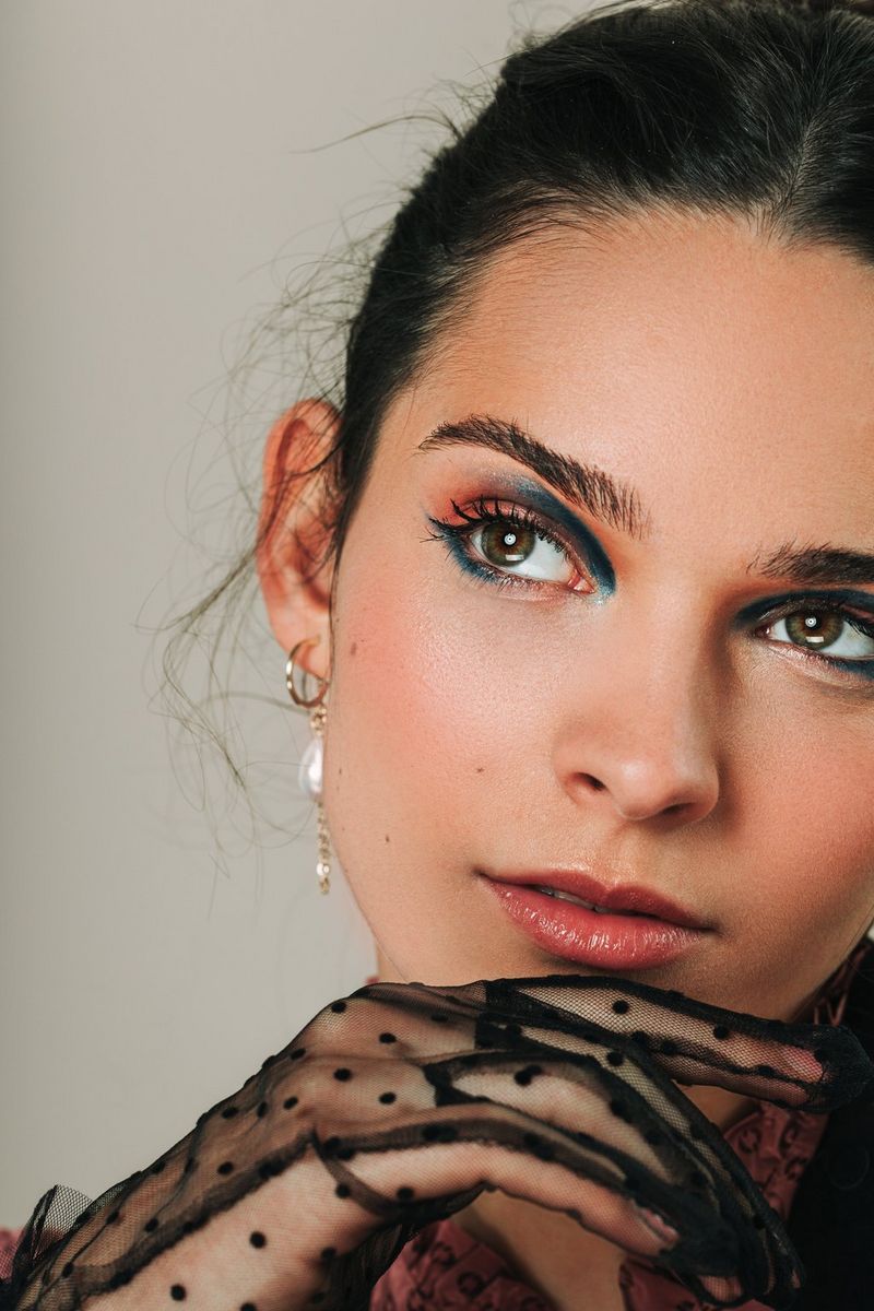 A portrait of a female fashion model posing with her head tilted slightly to one side and her chin resting on her lace-gloved hand.