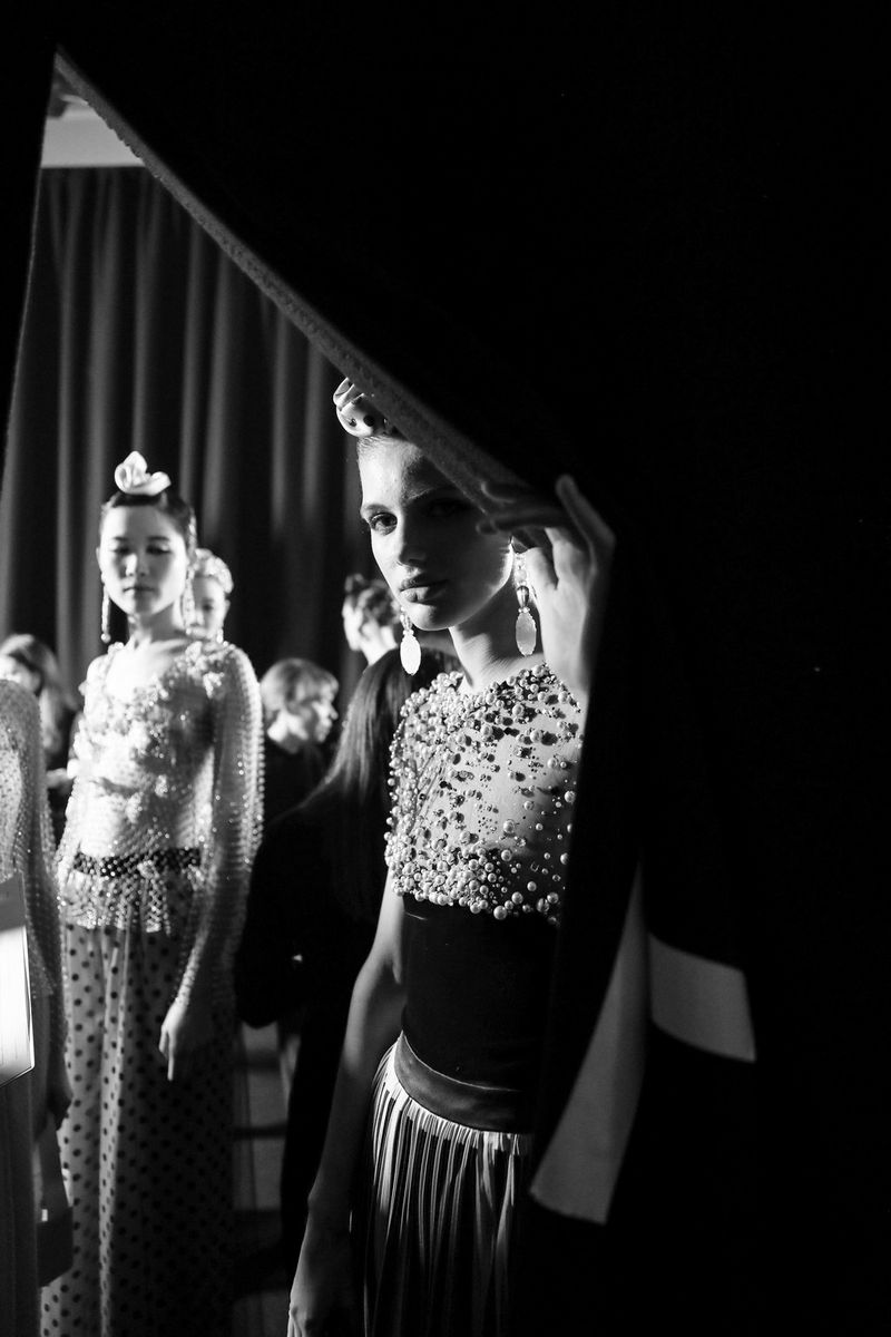 A black-and-white shot of models peering around a curtain. 